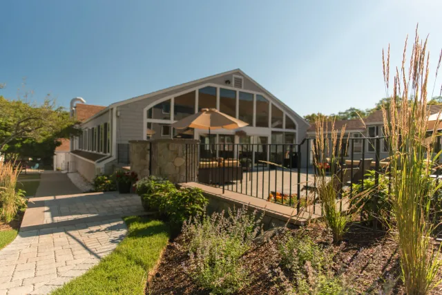 A residential house with a backyard patio, large windows, and a umbrella, surrounded by gardening and landscaping.