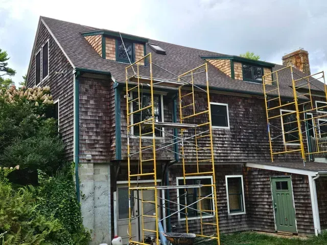 House exterior with yellow scaffolding and workers’ platforms under a cloudy sky