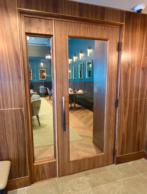 A wooden sliding door with a glass panel reveals a restaurant interior with tables, chairs, and blue walls decorated with framed pictures.