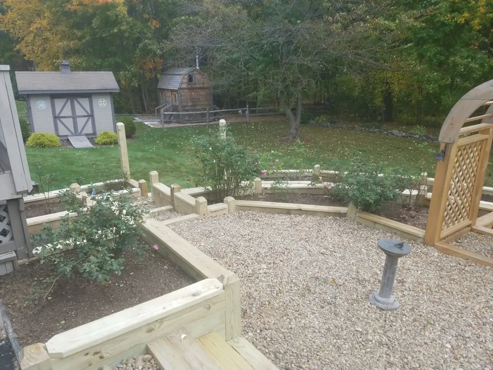 Backyard garden with gravel path, raised flower beds, a small shed, and a trellis arch.