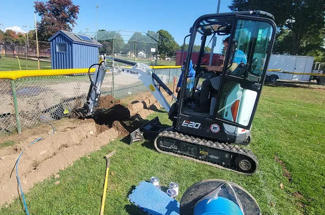 A man is driving a small excavator in a park.