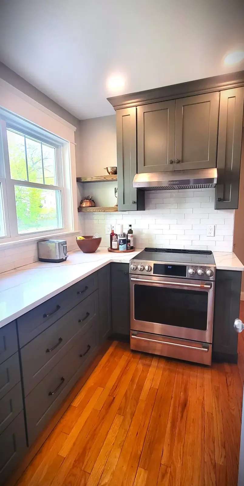 Interstate Custom Kitchen & Bath, Inc installs quartz countertops in a modern kitchen with dark green refaced cabinetry, stainless steel appliances, and white subway tile backsplash