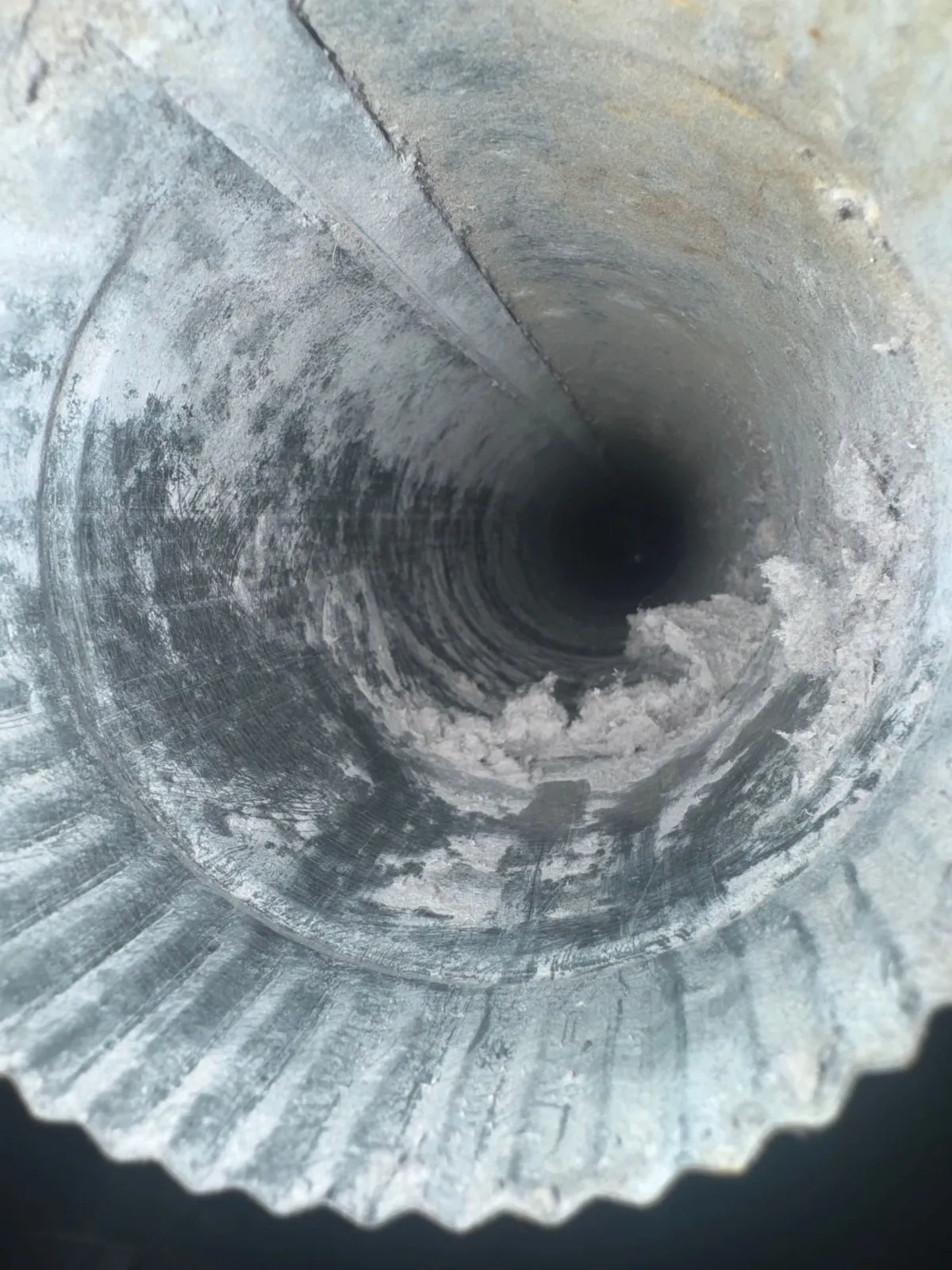 Interior of a ribbed dryer duct lined with lint and dark residue, the passage narrowed to a fraction of its width.