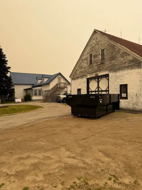 Historic stone building with dark dumpster in gravel lot under hazy sky