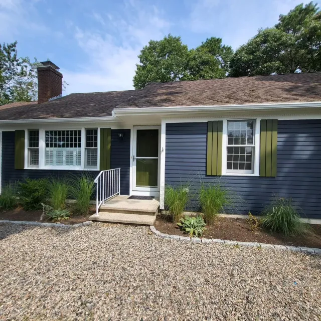 A blue house with green shutters and a gravel driveway