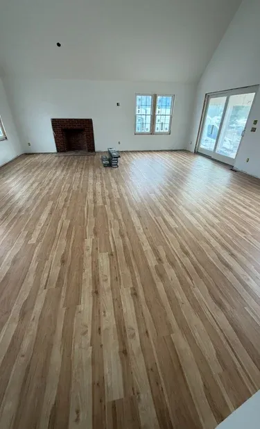 Spacious living room under renovation featuring new light oak hardwood flooring, a red brick fireplace, and vaulted ceilings.