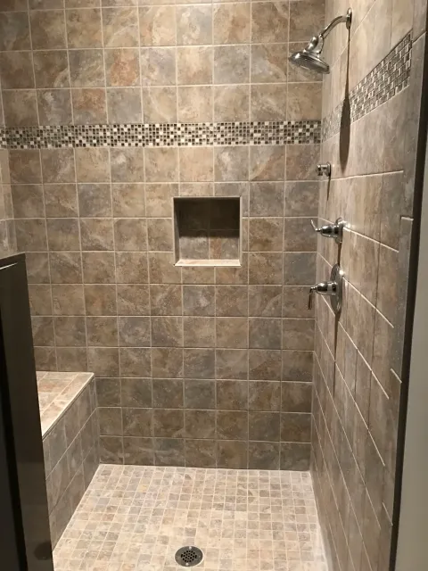 A tiled walk-in shower with a built-in bench, a small square niche, a rain shower head, and two adjustable body spray nozzles.