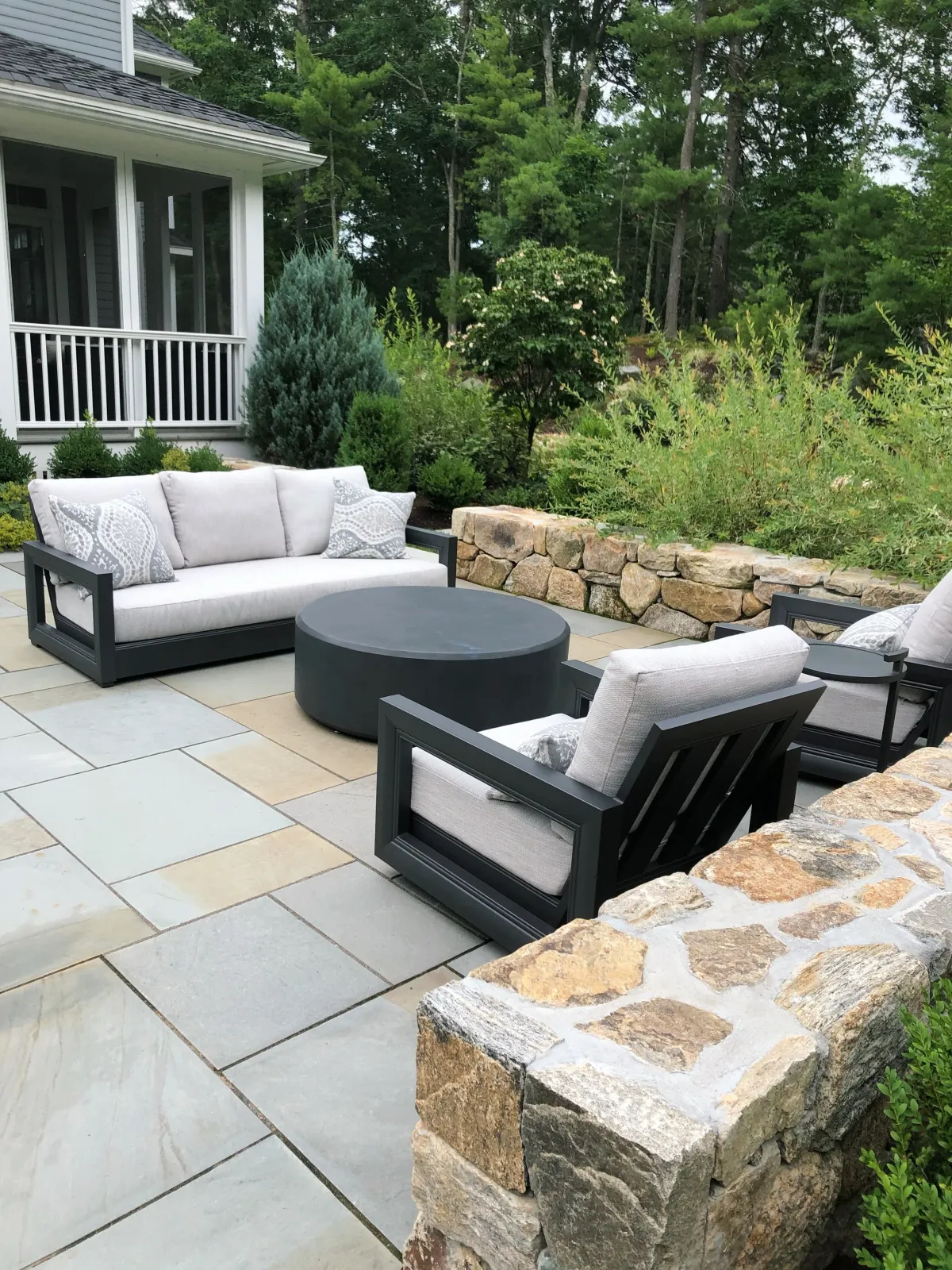Stone sitting walls frame a blue stone patio and outdoor entertainment space that gives this Boxford home an amazing outdoor room to enjoy while offering four seasons of garden interest.