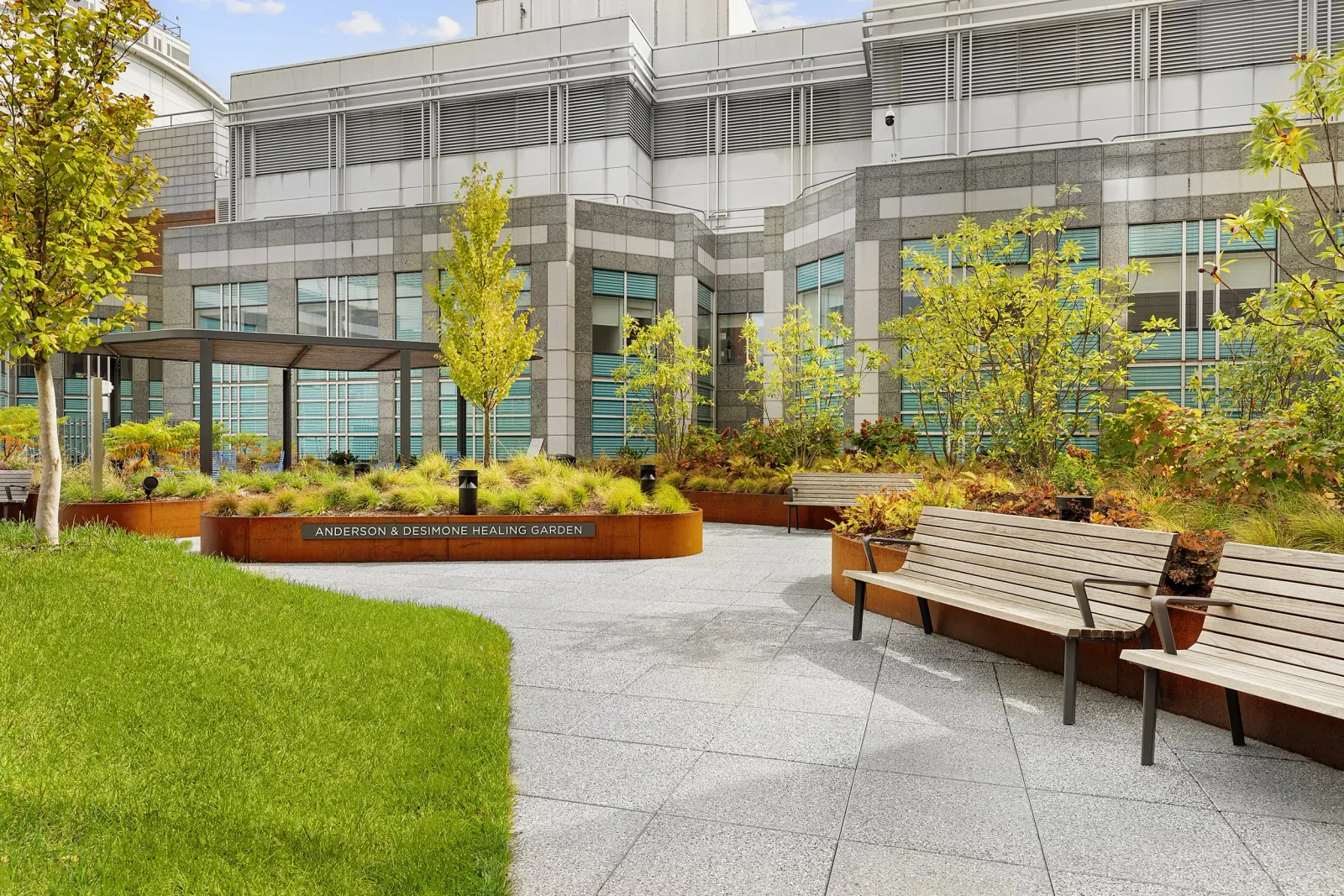 Outdoor Rooftop Healing Garden area with benches, trees, plants, and a sign that reads 'Anderson & Desimone Healing Garden' in front of the new Beth Israel West Campus Impatient Building.