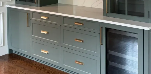 Brass pulls on green painted drawer fronts under a stone counter