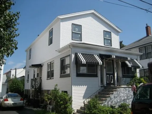 Two-family exterior with new siding, porch and striped awnings