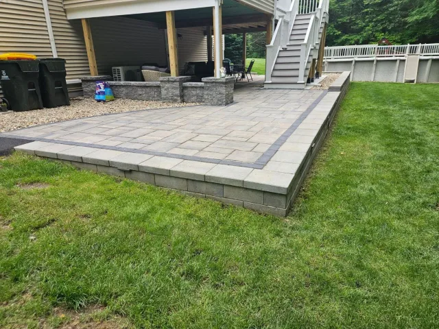 A patio with a staircase leading up to it is in the backyard of a house.