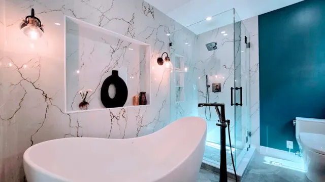 Modern bathroom remodel in Avon, CT with a white bathtub, glass shower, teal accent wall, and marble-like walls.