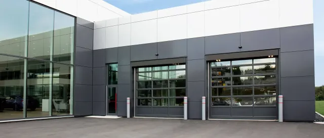G-4400 commercial glass garage doors (12×12) with Iron Ore frames, installed on a modern commercial building in Lincoln, RI by Quality Overhead Doors