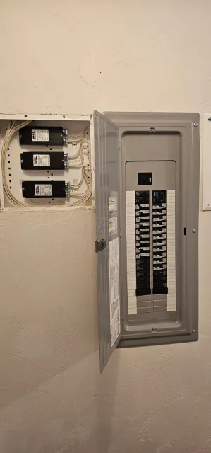 Open electrical breaker panel with three breakers in a wall alcove