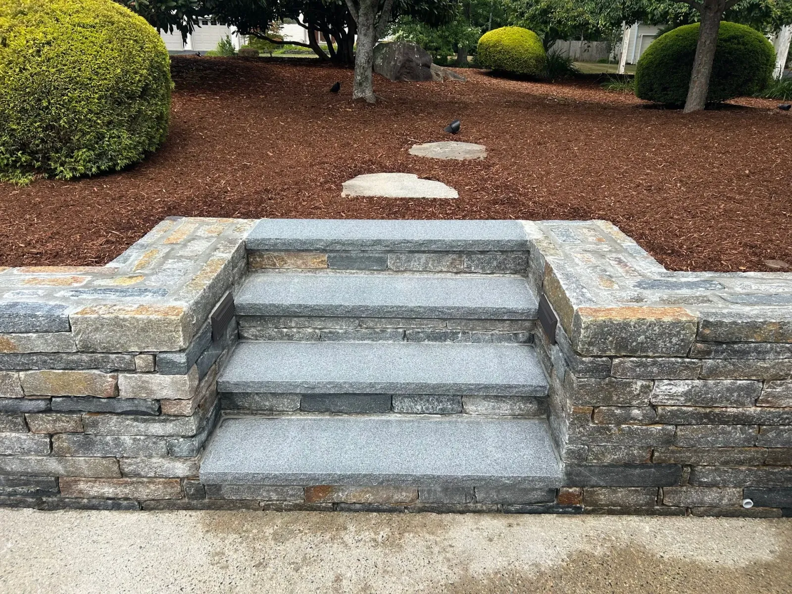 Stone steps in a landscaped garden with mulch, shrubs, and stepping stones leading upward