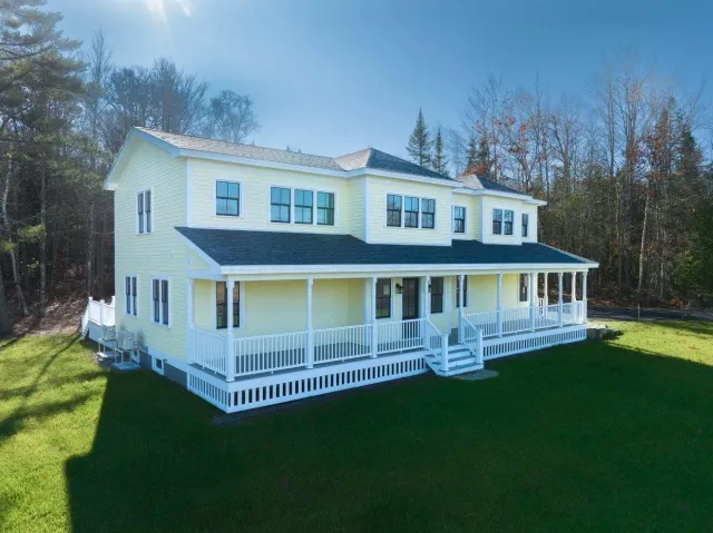 A large yellow custom built house with a large porch is sitting on top of a lush green field.
