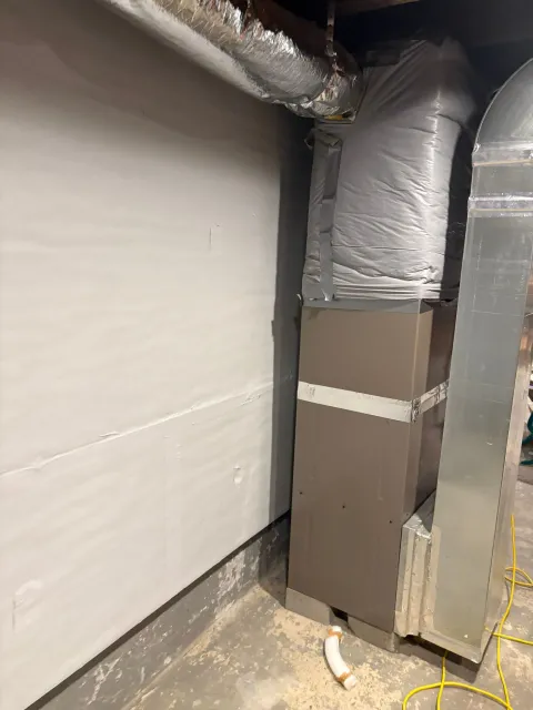 Basement corner with insulated ductwork, white wall, and exposed piping on a concrete floor