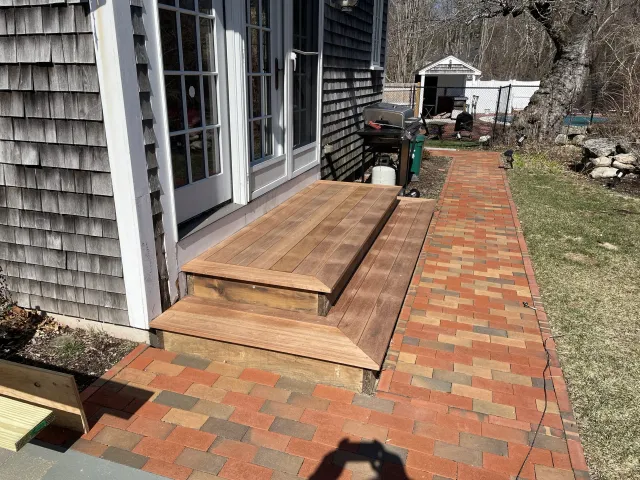 Backyard with brick patio, wooden deck, and sliding glass door.