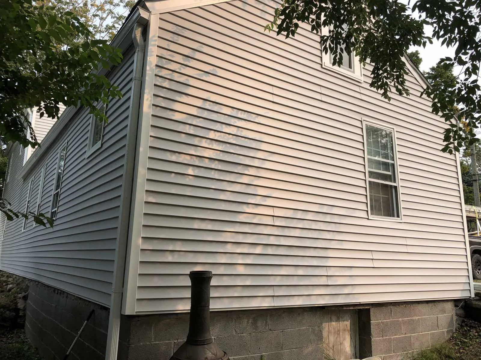 The side of a house with light gray horizontal vinyl siding, a small window, and a dark concrete block foundation.
