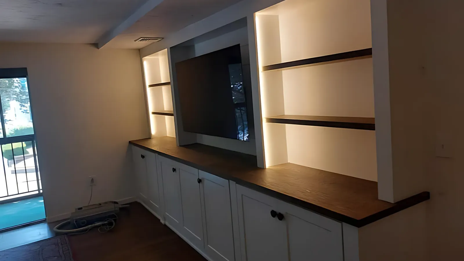 Built-in wall cabinet with wood countertop, shelves, and lower cupboards in a dimly lit room