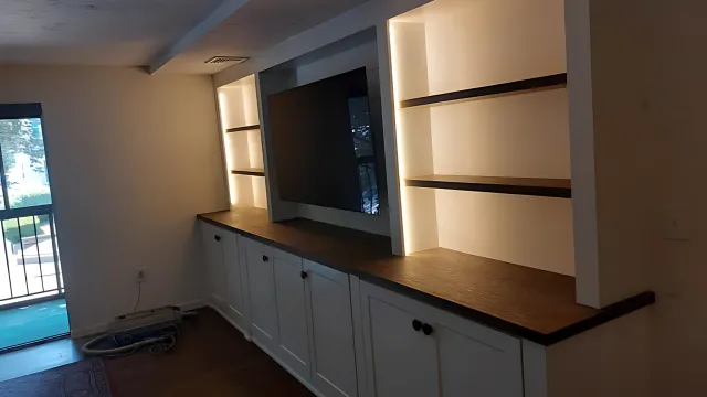 Built-in wall cabinet with wood countertop, shelves, and lower cupboards in a dimly lit room