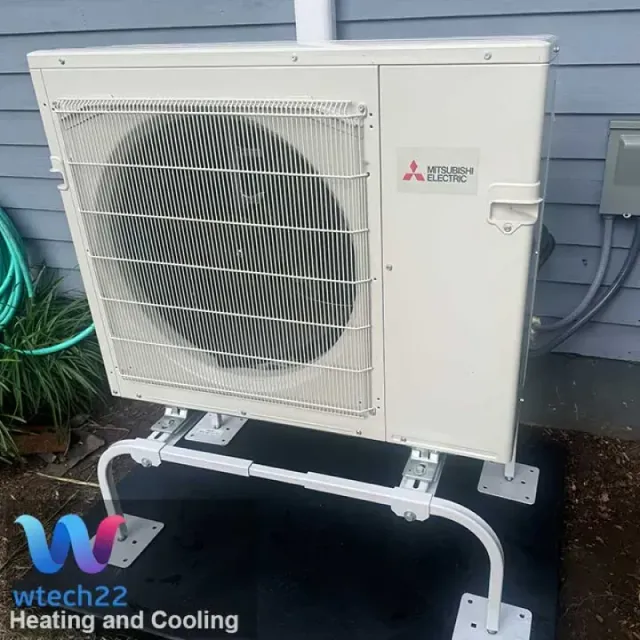 Mitsubishi Electric heat pump unit on white metal stand, next to a building.