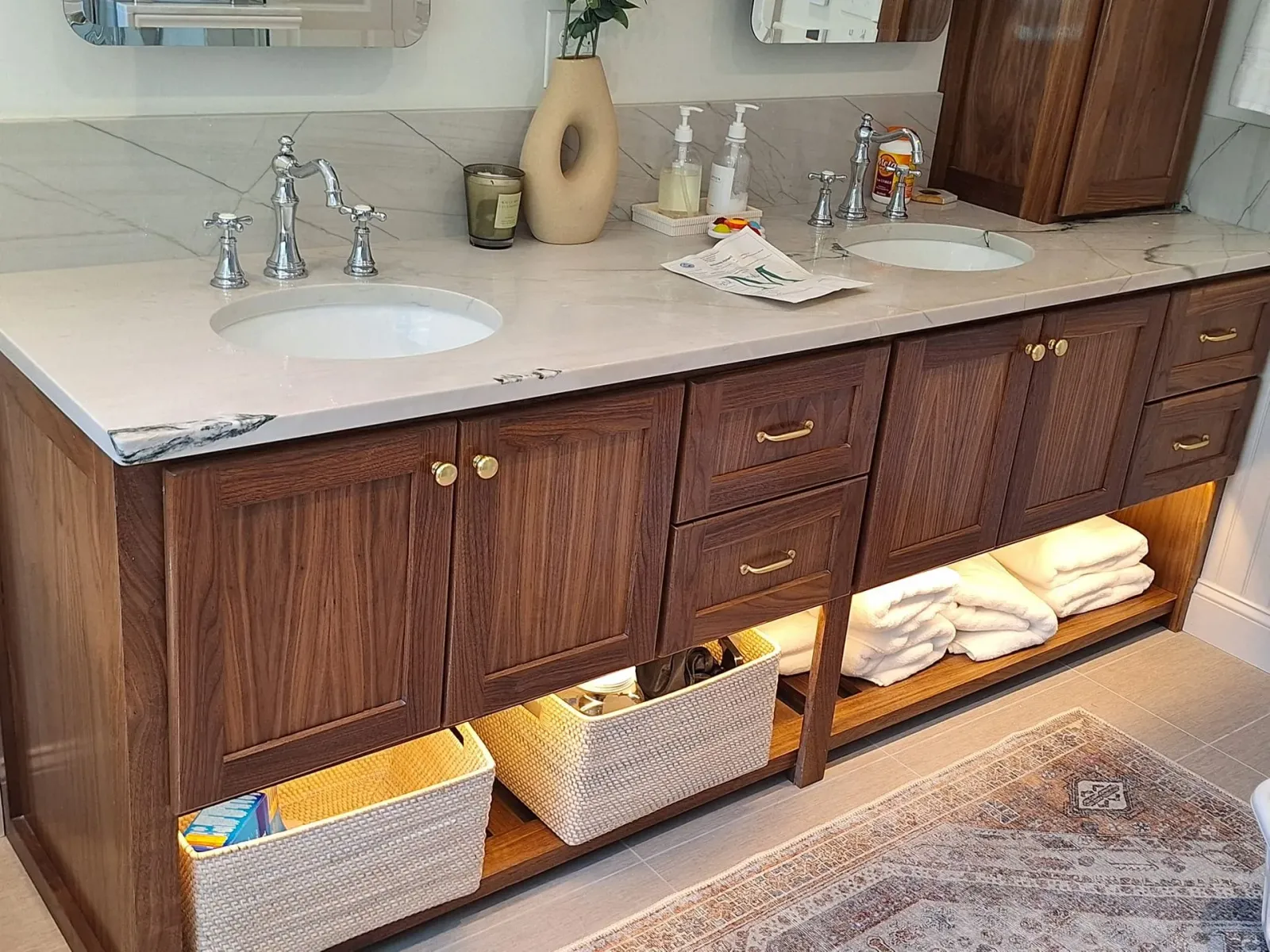 Bathroom vanity with double sink, wooden cabinets, woven storage baskets, and towels underneath.