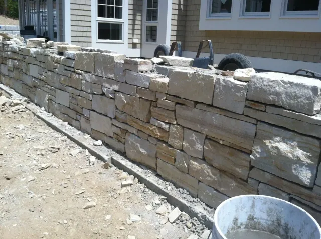 A stone wall is being built in front of a house