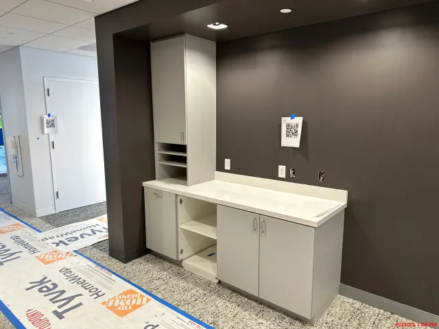 Modern office break room with gray cabinets, white countertop, and dark accent wall.