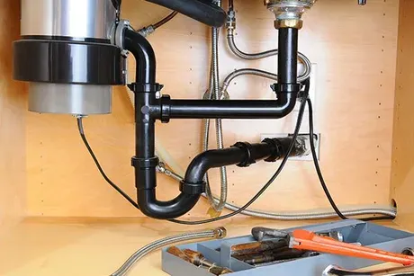 A sink with a garbage disposal and a wrench underneath it.
