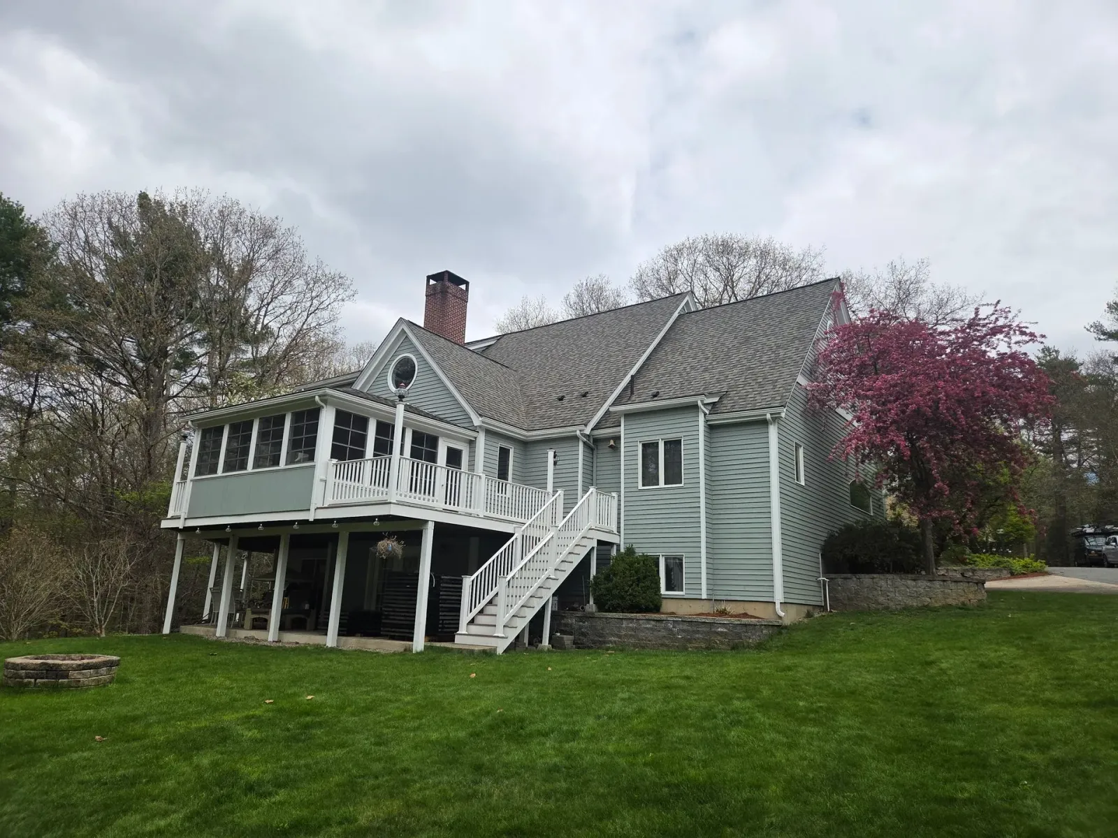White farmhouse-style house with porch and stairs on a green lawn under cloudy skies