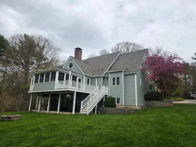 White farmhouse-style house with porch and stairs on a green lawn under cloudy skies