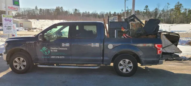 Blue pickup truck with company logo, loaded with equipment in the bed, parked outdoors in a lot.