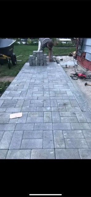 A man is laying bricks on a sidewalk in front of a house.