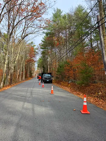 Utility truck and orange cones on a wooded road in autumn