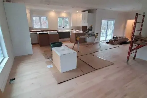 open-concept kitchen and living area showing newly installed light hardwood flooring protected by cardboard sheets during active home remodeling
