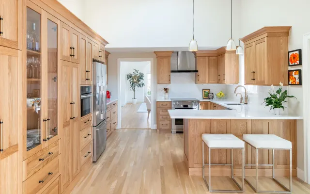 Bright modern kitchen with light wood cabinets, island stools, and stainless steel appliances