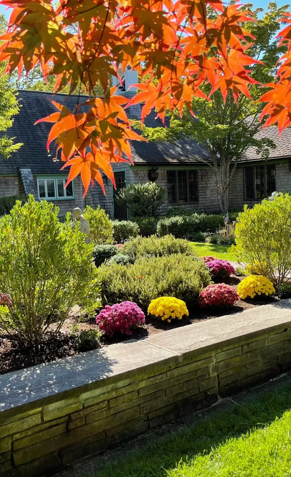 Autumn foliage frames a stone building with a flower garden.