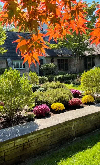 Autumn foliage frames a stone building with a flower garden.