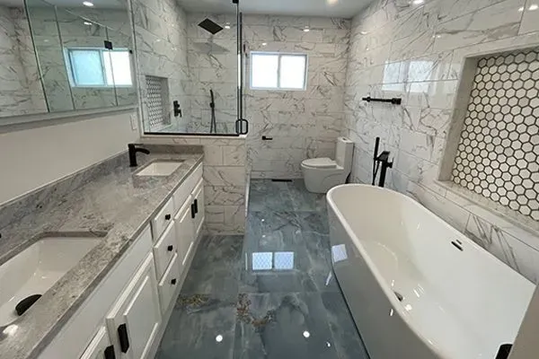 Modern bathroom with white and gray marble tile, blue floor tile, soaking tub, and double vanity.