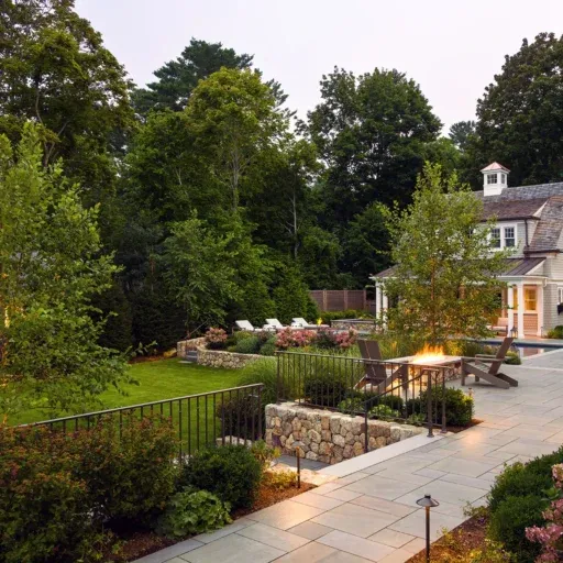 A Wayland bluestone terrace with evening lighting and a fire feature turns a sloped property into a warm, elevated outdoor living area.