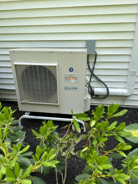 Outdoor air conditioning unit installed outside house with green shrubbery in front.