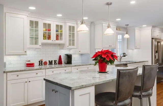 Kitchen renovation with white shaker cabinetry, subway tile backsplash, marble-look countertops, glass-front upper cabinets, and a contrasting gray island with upholstered stools.