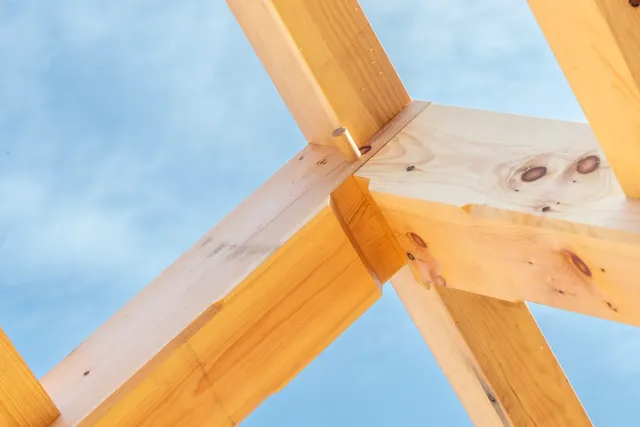 Close-up view of wooden construction beams joined together with visible nails, against a blue sky background.