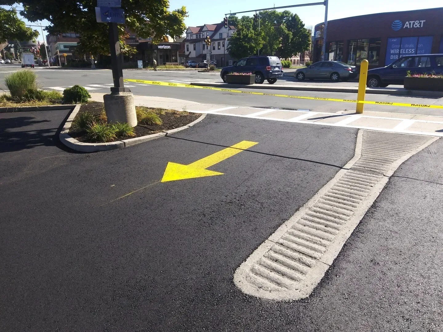Crosswalk curb ramp at a street corner with a yellow directional arrow and bollard