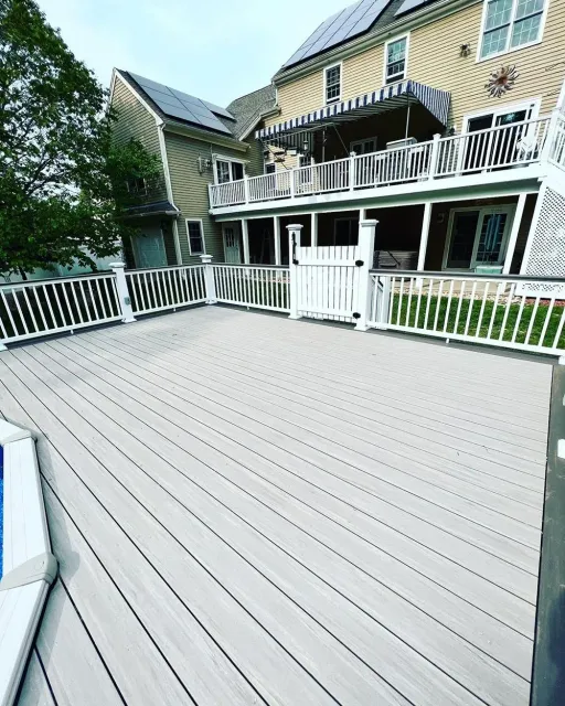 A large deck with a white railing and a house in the background