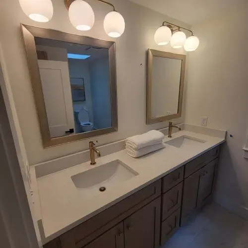 A bathroom with two sinks , two mirrors and a toilet.
