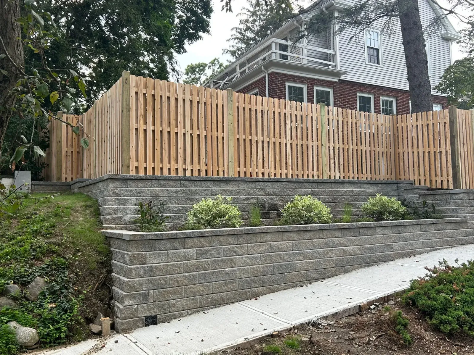 A wooden fence surrounds a stone wall in front of a house.