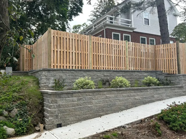 A wooden fence surrounds a stone wall in front of a house.